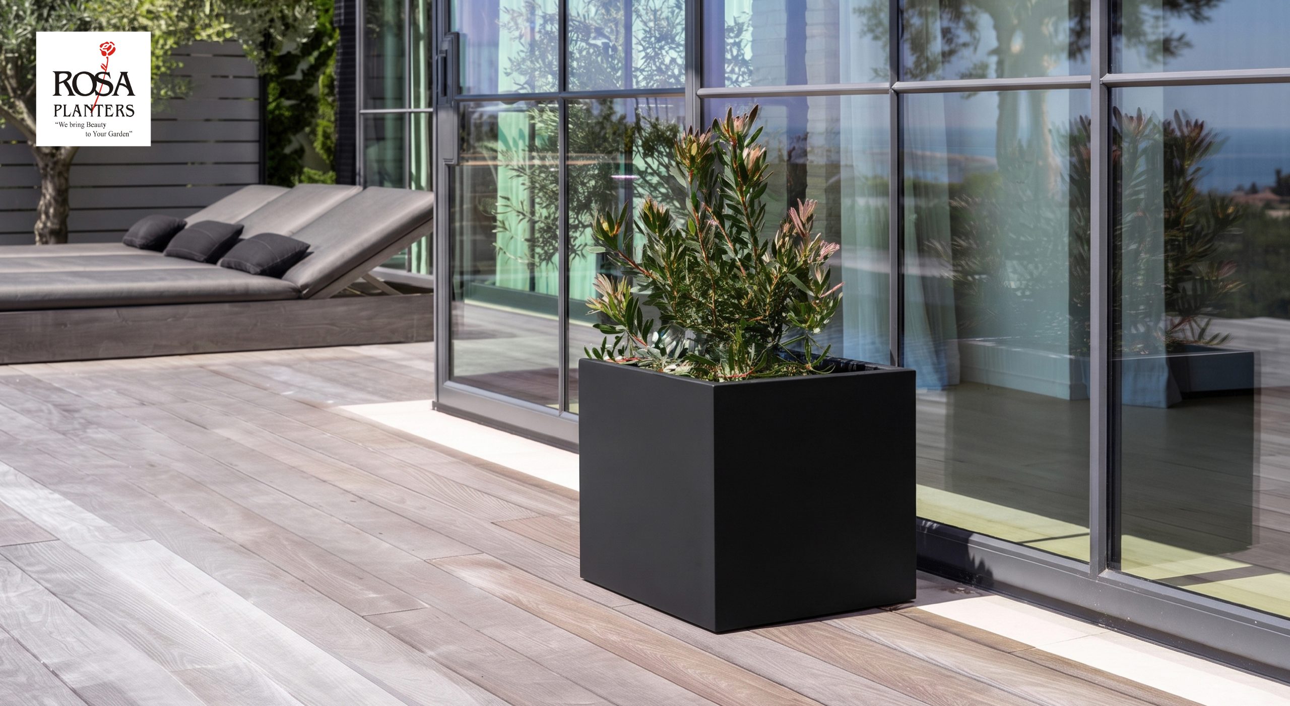 Black square polystone planter with sharp edges on a wooden terrace beside glass doors